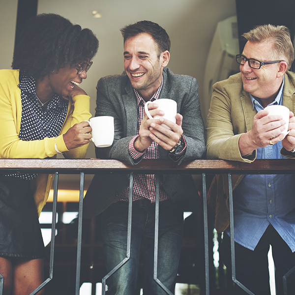 Three people standing together holding coffee cups and laughing